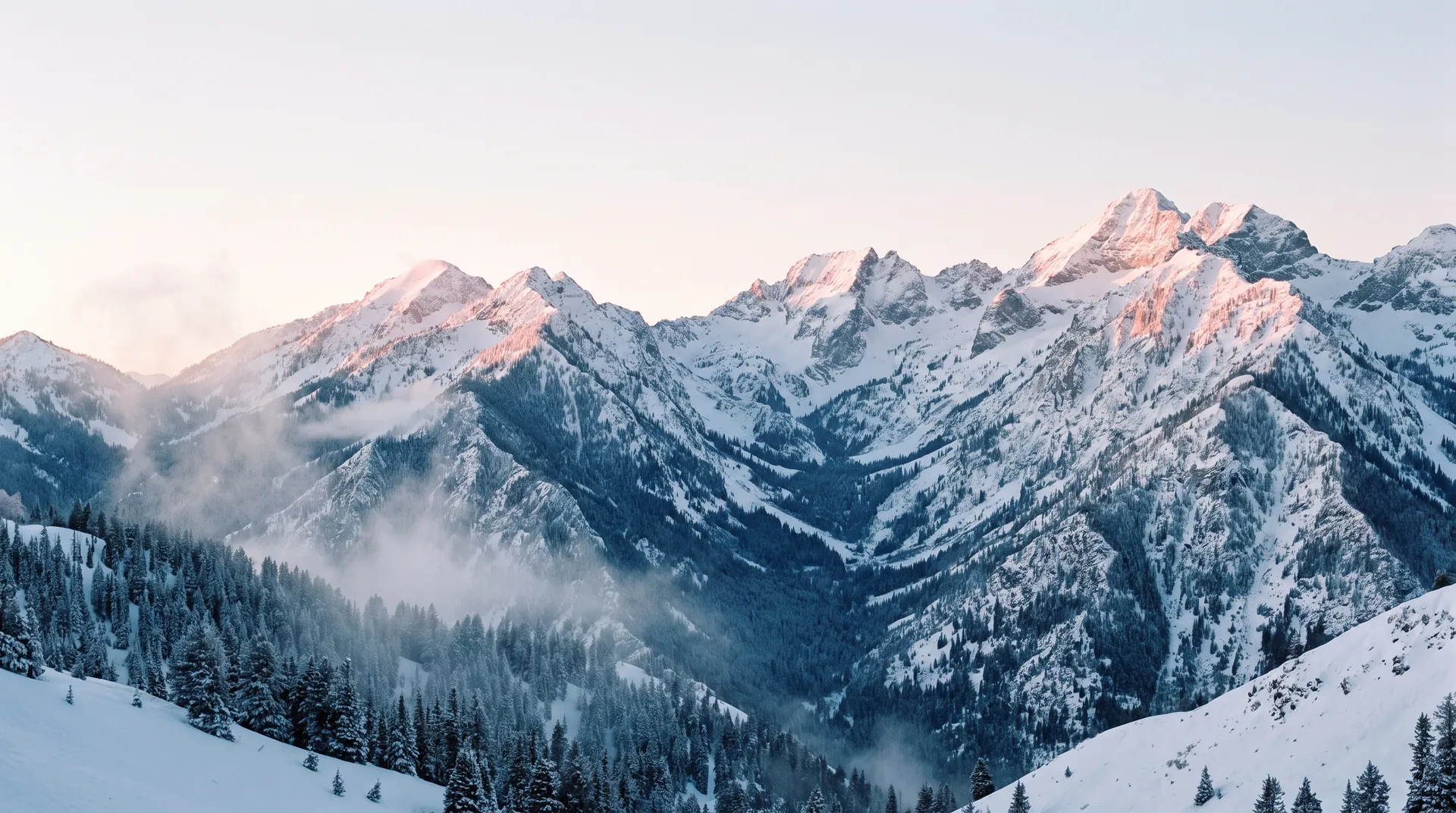 Snow-covered Wasatch peaks at blue hour, alpenglow on the summits and mist rising from the forested valley below